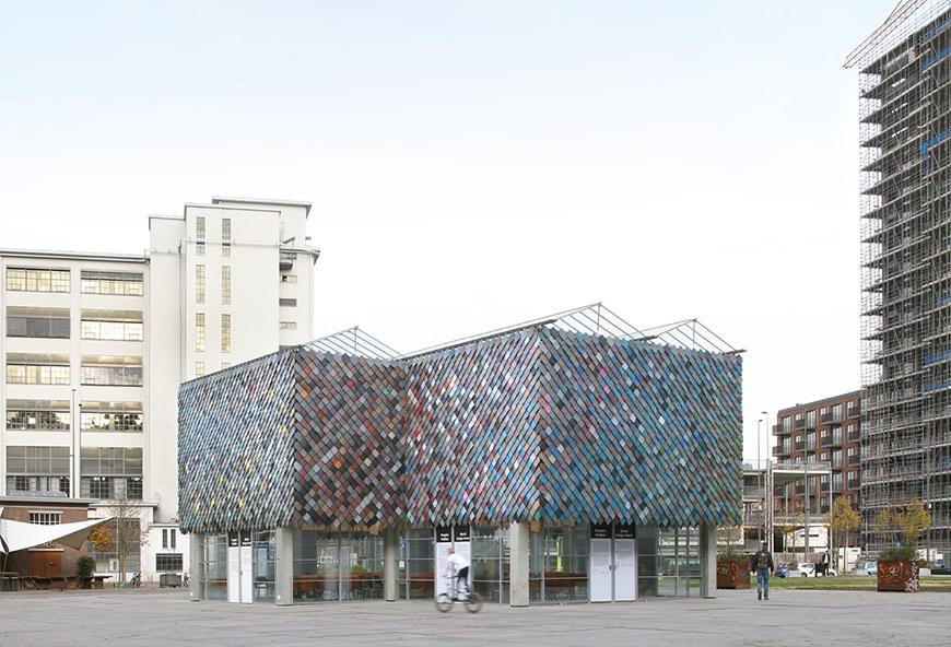 A pavilion with a pixel-like mosaic facade made from recycled plastic materials of varying colors. 