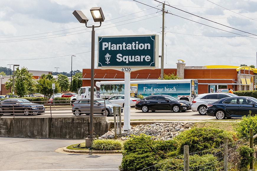 A parking lot with a large sign that says plantation square and a building in the background.