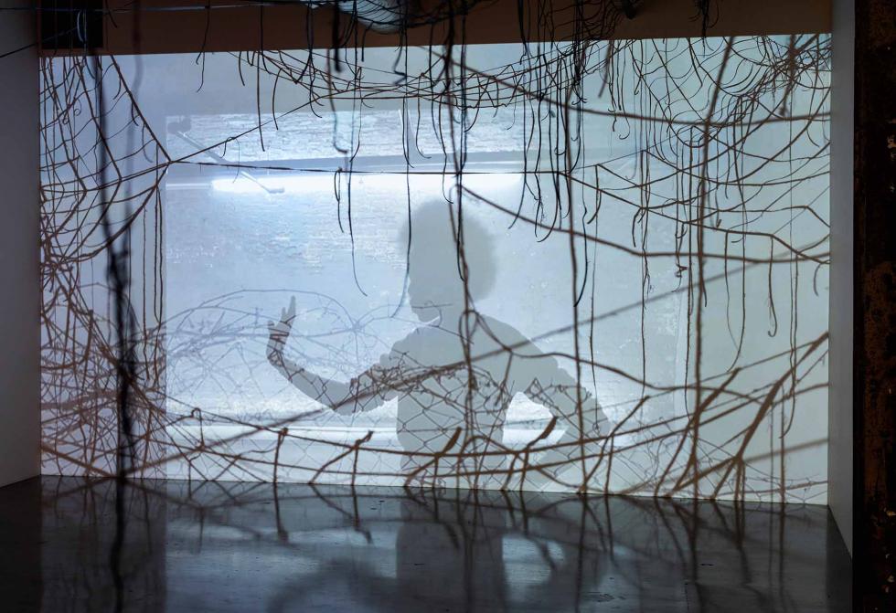 Shadow of a person with their hand up on a light colored background with strings.