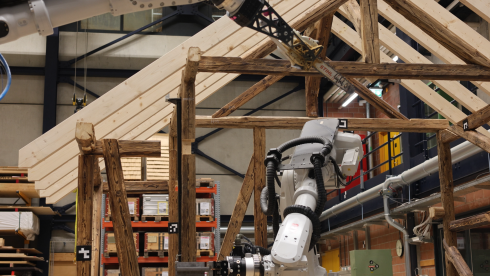 Robotic arms sustaining a structure made of wooden beams.