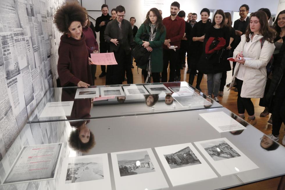 A woman points to a discplay of documents in front of a group of students