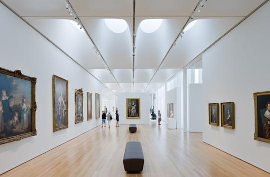view of an art gallery interior with benches on a wood floor and paintings on three walls