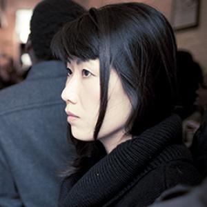 profile of a woman's face with long dark hair and a person behind her