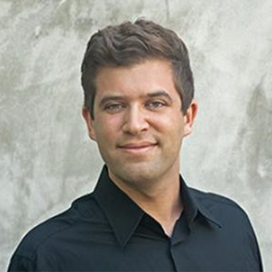 A man with a dark blue shirt smiles at the camera.