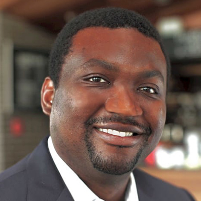 Black man with short dark hair wearing a white shirt and grey suit jacket